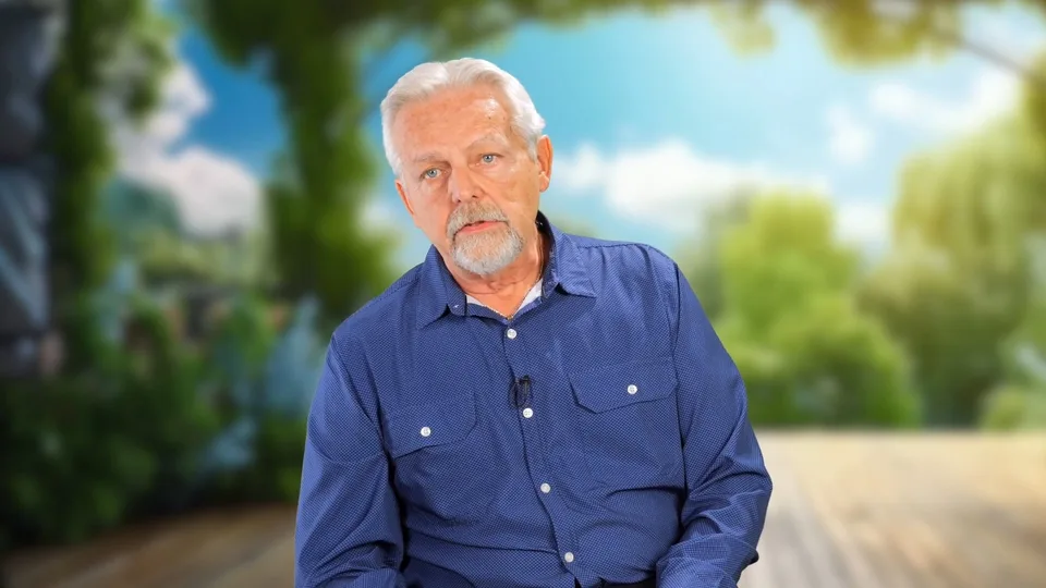 Roland Verfaillie in a blue shirt, seated for an on-camera interview with trees behind him